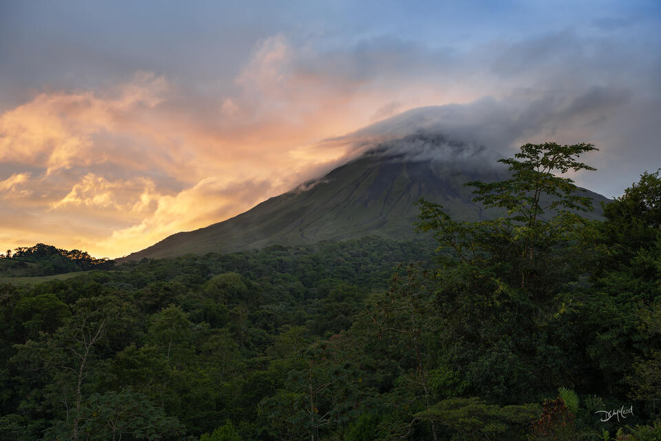Arenal volcano in Costa Rica at sunrise with colorful orange clouds.