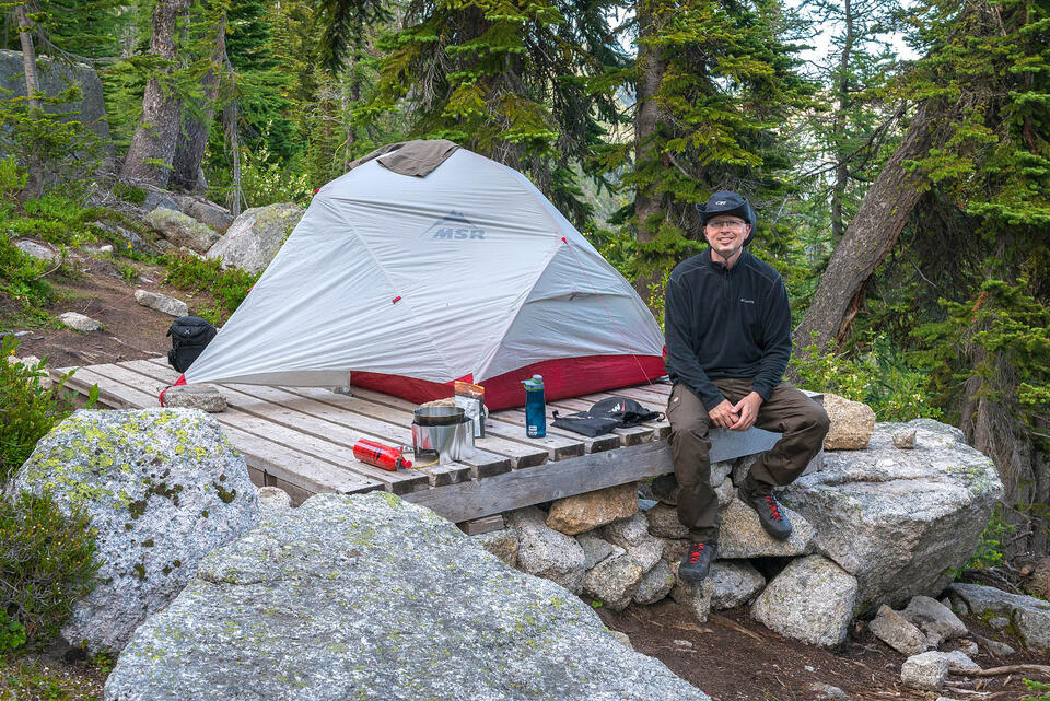 Man sitting outside beside ground tent in the mountains.