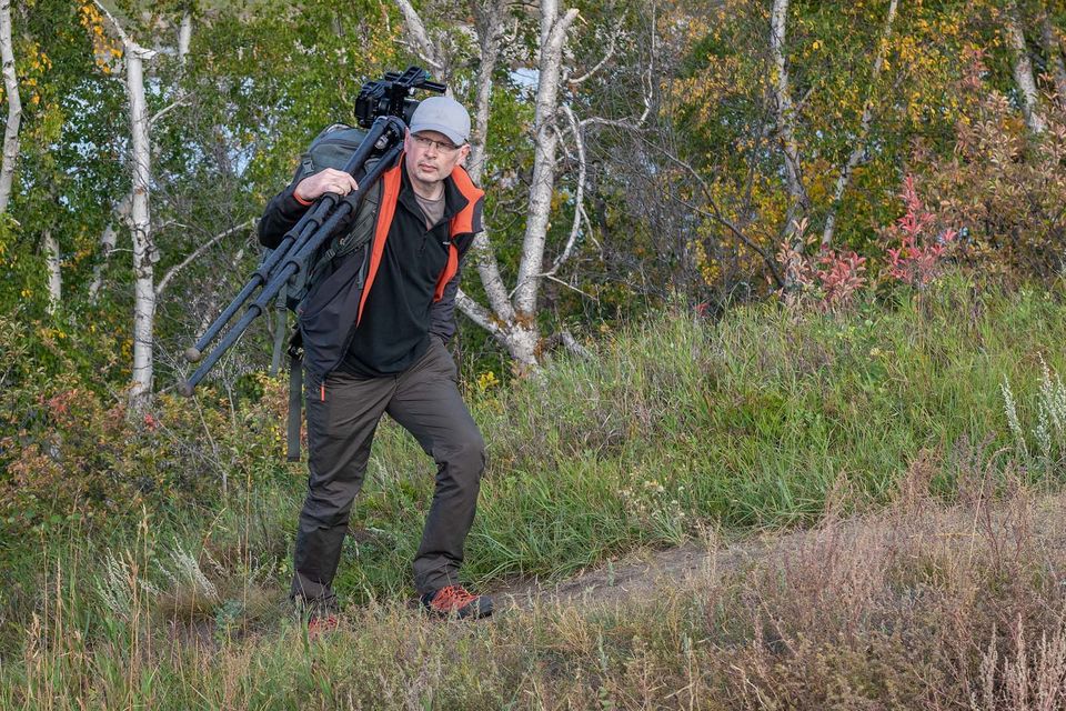 Photographer walking up hill with tripod perched over shoulder.