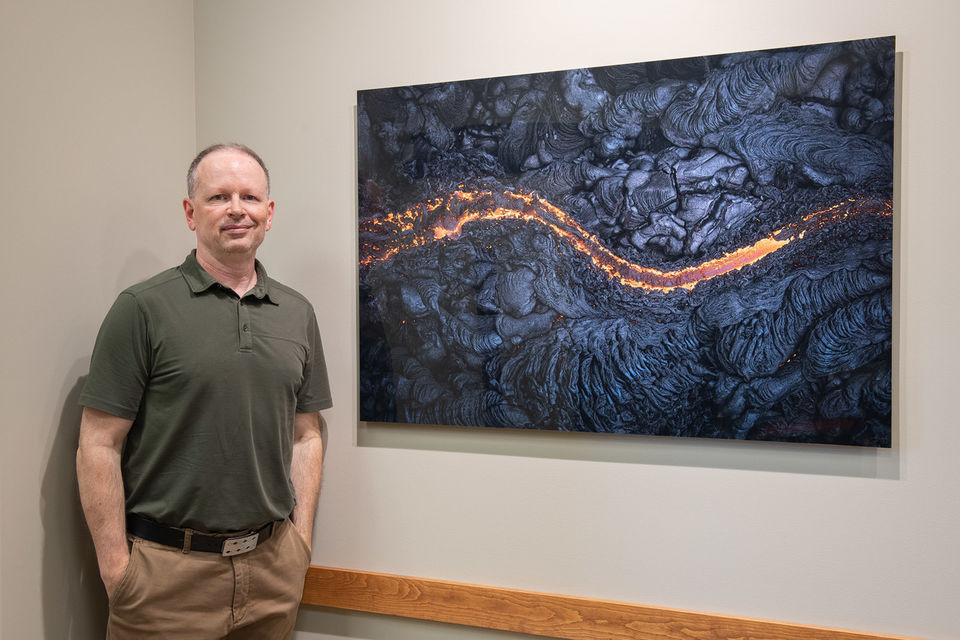 Man posing beside metal print of lava hanging on wall.