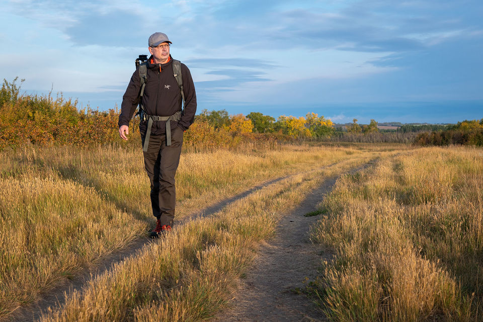 Man with backpack walking on trail at sunrise.