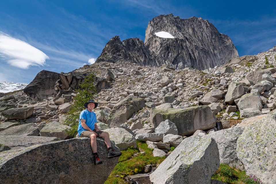 Man posing sitting on huge boulder in mountains.