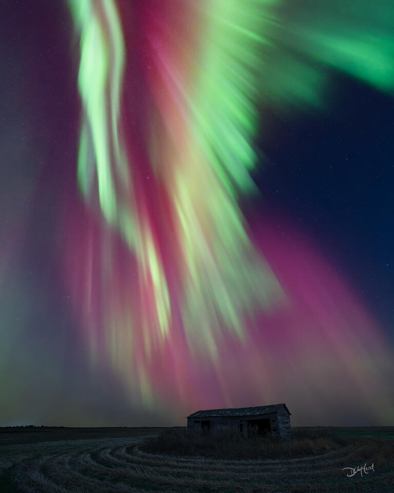 Aurora borealis shaped like wings over prairie farm building in Saskatchewan, Canada.