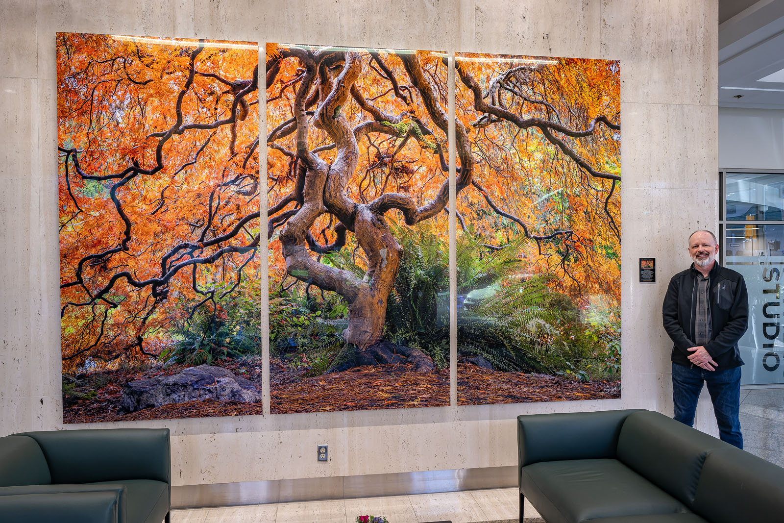 Dean McLeod standing beside an 8×12-foot Lumachrome® TruLife® acrylic triptych in an office tower lobby.