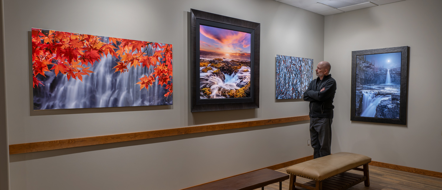 Dean McLeod in his fine-art photography showroom with four prints illuminated by LuxPrism.
