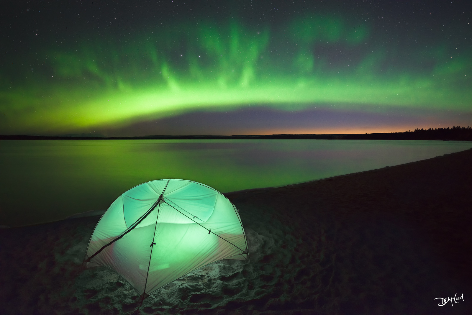 Nighttime view of a small tent on the beach of a lake with the aurora borealis and stars in Saskatchewan, Canada.