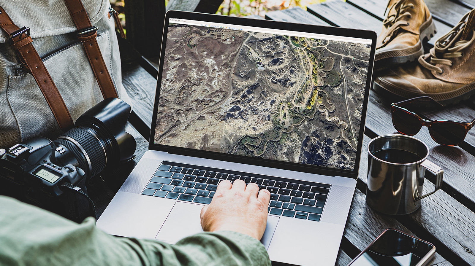 Landscape photographer studying Google Earth on laptop with camera gear on a desk.