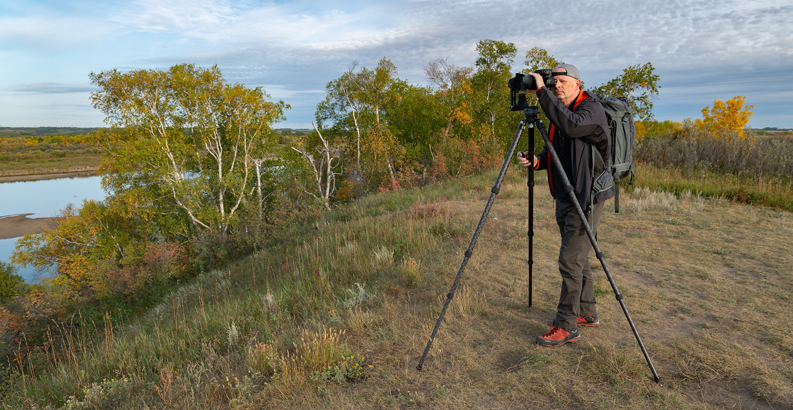 Photographer with tripod on a Saskatchewan riverbank in autumn.
