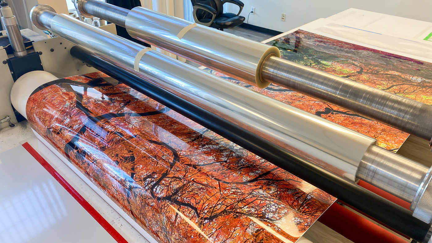 Lumachrome photographic layer passing through rollers as adhesive is applied for acrylic face mounting.