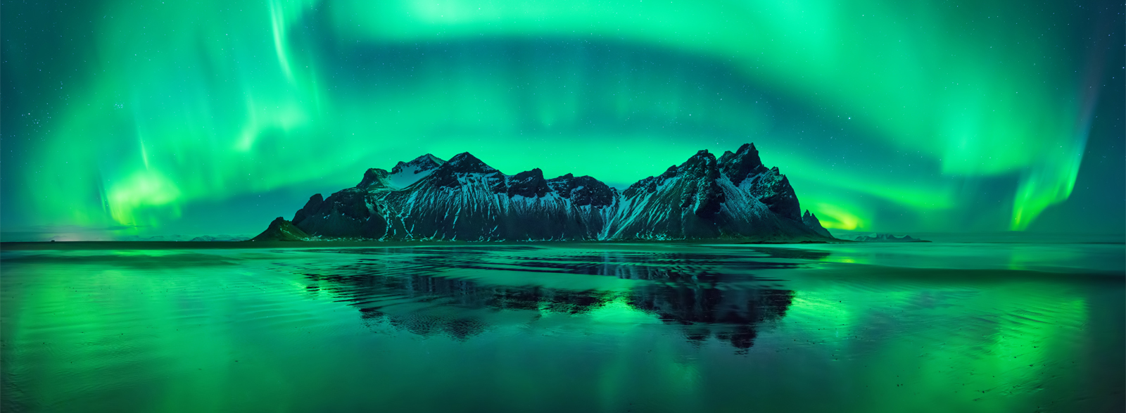 Vestrahorn mountain in Iceland in the winter at night with bright green aurora.
